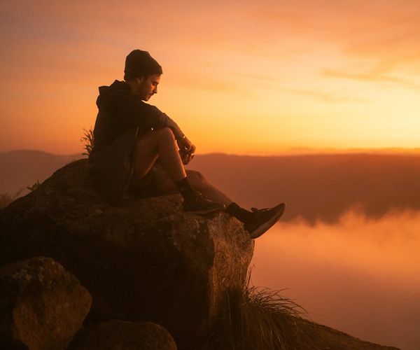 Person meditating peacefully at sunrise with a calm mountain view.